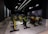 A dimly lit indoor cycling studio with multiple stationary bikes arranged in rows. The bikes have bright colors, including yellow, red, and green, contrasting with the dark walls and ceiling. The room has a modern, industrial feel with metal panels along the lower walls and sleek overhead lighting.