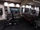 A gym with an array of dumbbells neatly organized on racks in front of large mirrors, with various strength training equipment including a bench press visible. The lighting is subtle and modern, with black and metallic gray tones dominating the space.