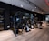 A modern gym setting filled with exercise machines such as ellipticals, stationary bikes, and weightlifting equipment. The room features a sleek design with dark walls, wooden flooring, and a mirrored wall that enhances the spacious feel. Ceiling lights provide illumination, creating an inviting atmosphere for workouts.