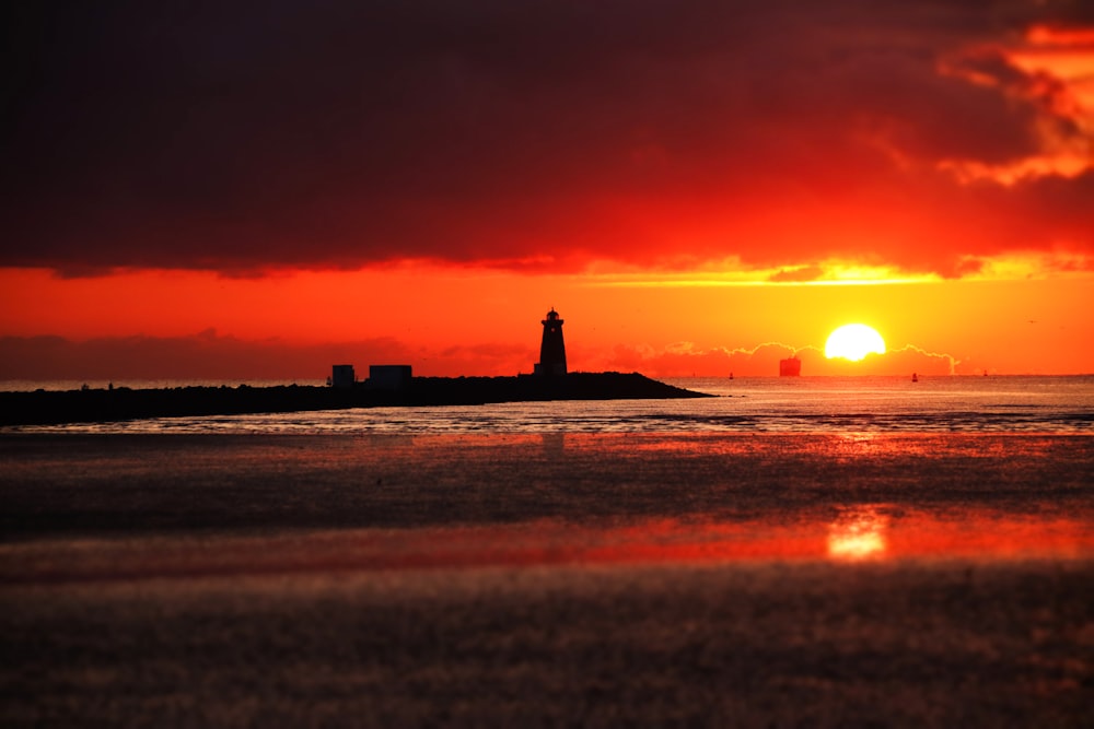 the sun is setting behind a lighthouse on the water