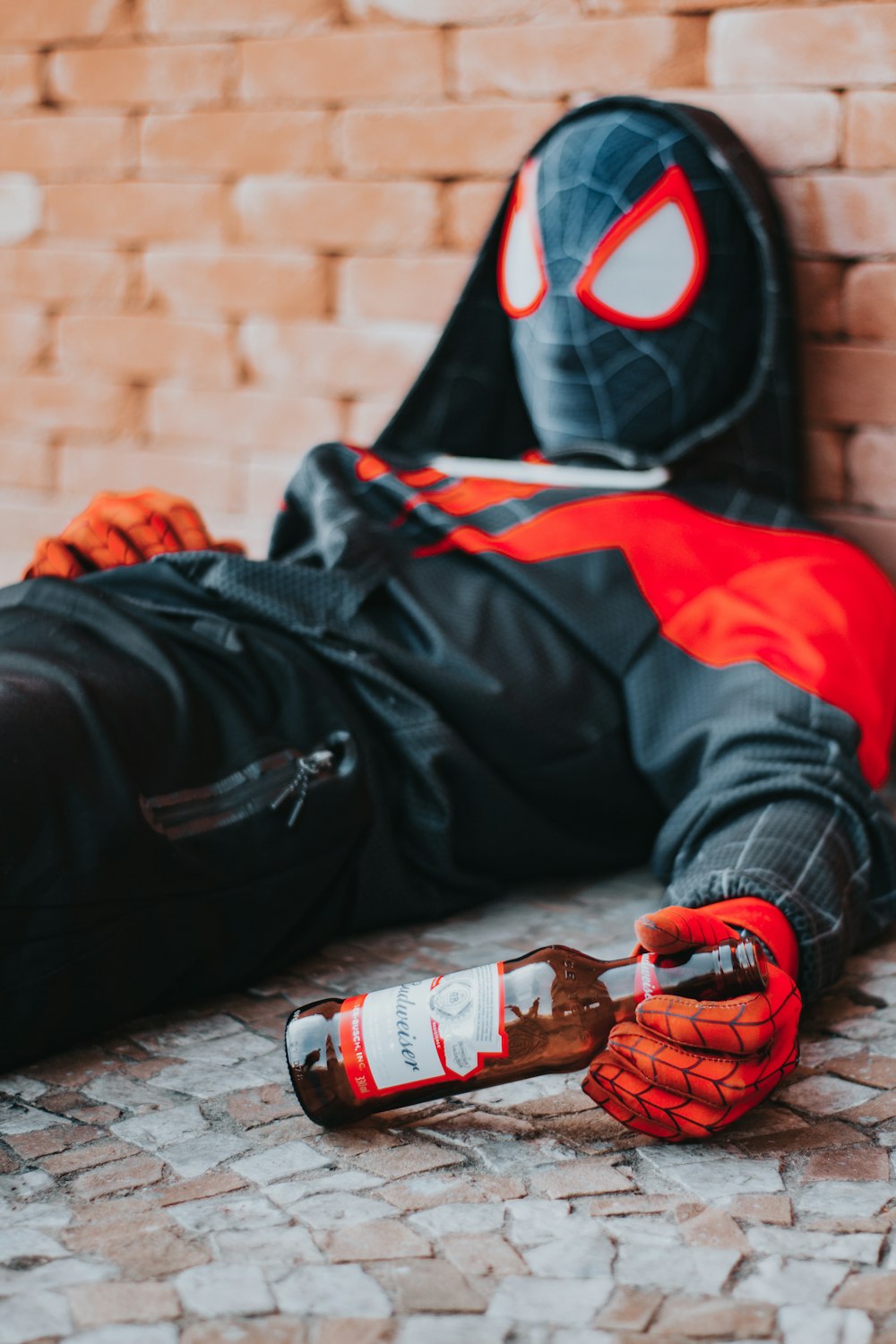 a person in a spider suit laying on the ground with a bottle of beer