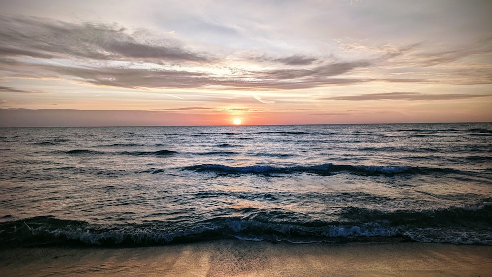 the sun is setting over the ocean on the beach