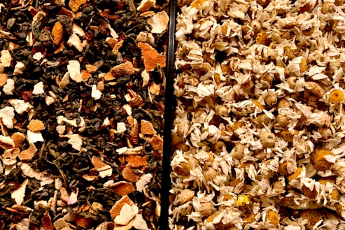 A close-up view of two different mixtures, separated by a vertical line. On the left, a blend of assorted dried leaves and orange peel in dark and light brown shades. On the right, dried chamomile flowers with pale yellow petals and light brown centers.