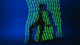 A dark silhouette of a person is seated against a deep blue background. Bright green text is projected onto the figure and the backdrop, creating an intricate pattern. The text includes words such as 'ERIC', 'MAGNA', and 'RAJ'. The lighting creates a mysterious and artistic atmosphere.
