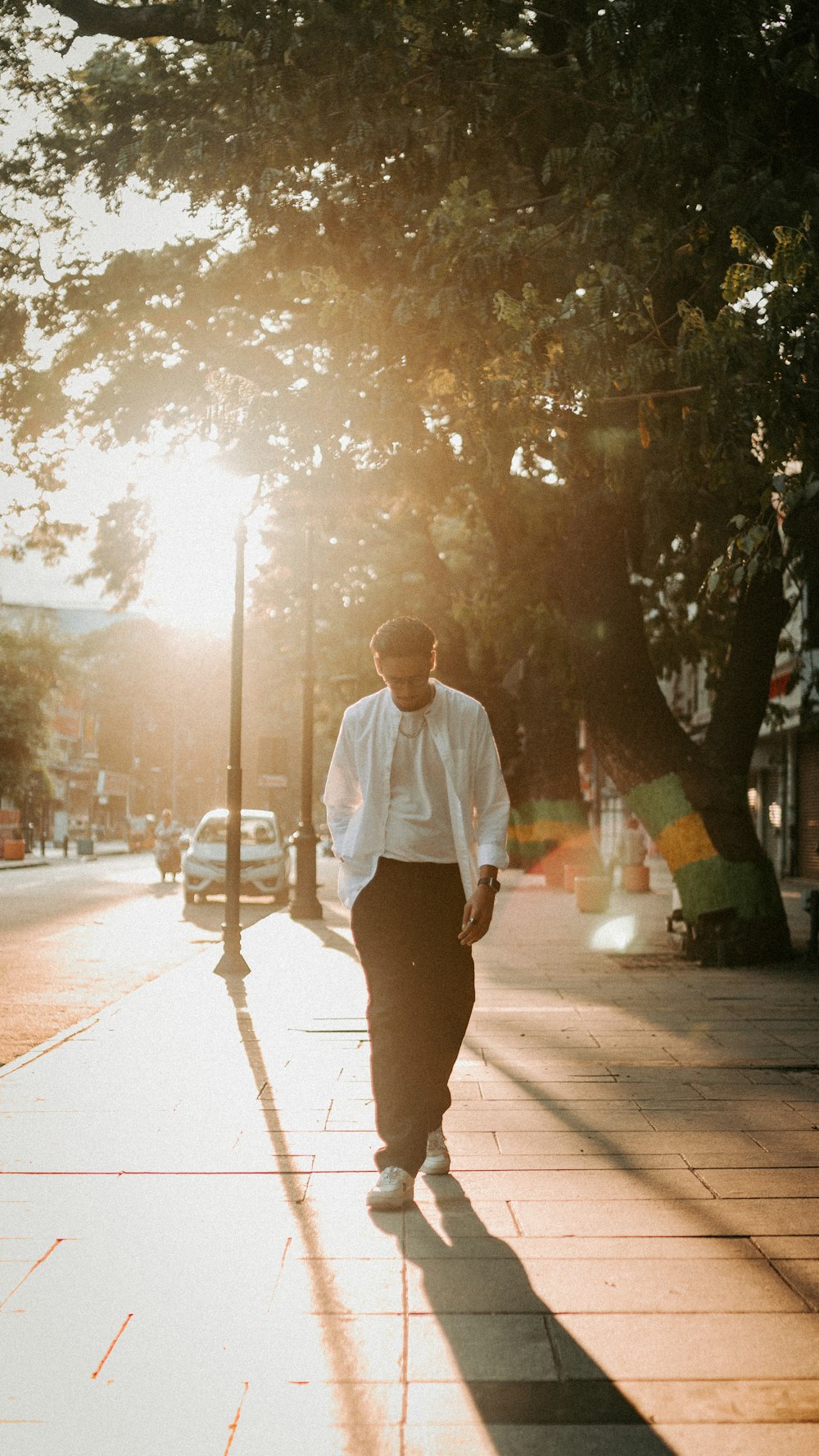 a man walking down a sidewalk next to a tree