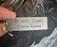A metal keychain is held between two fingers. It features the engraved text 'Be safe Come home' and an elegant decorative scroll design.