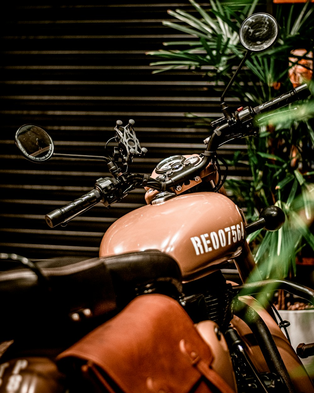 a brown motorcycle parked next to a green plant