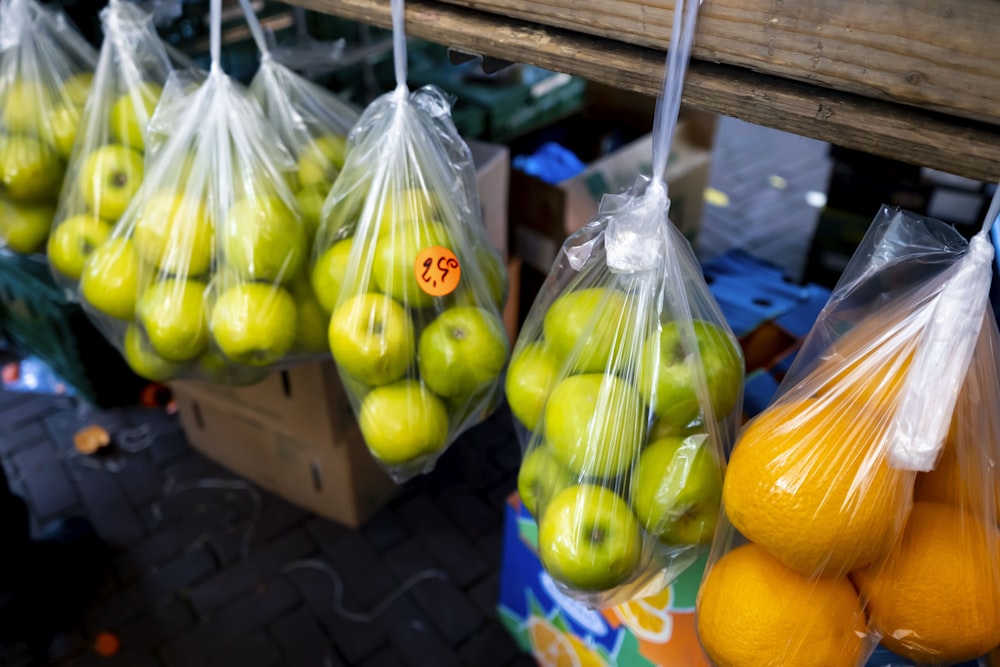 bags of green apples and oranges hanging from a rack