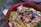 A vibrant bowl filled with fresh ingredients including cut salmon, avocado slices, edamame beans, corn, and drizzled with a dark sauce. The mixture is arranged in a red bowl on a rustic surface.