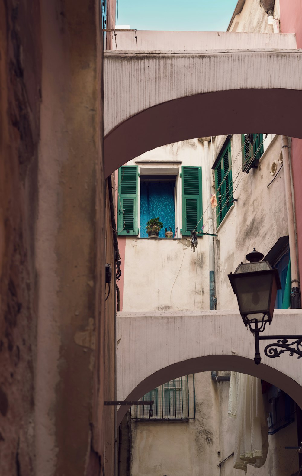 a narrow alleyway with a lamp post and green shutters