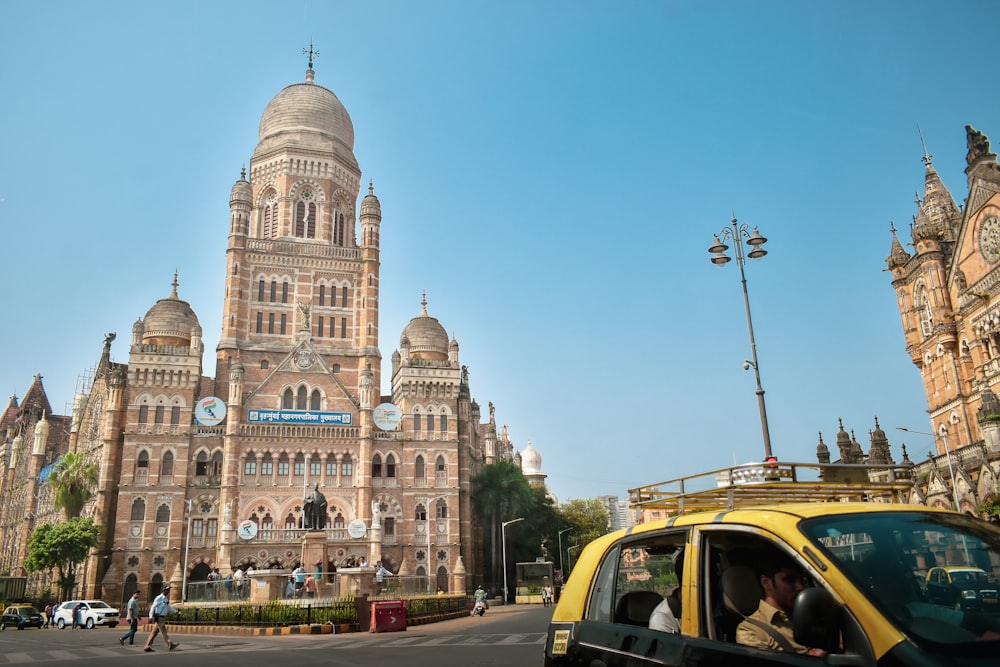 a yellow taxi driving past a tall building with a clock tower