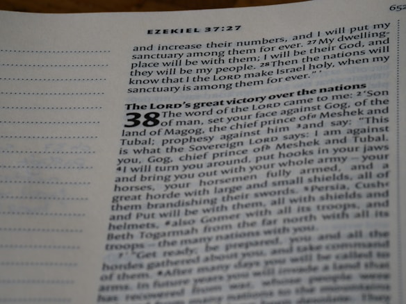 An open page from a Bible, displaying text from the book of Ezekiel, chapter 37 verse 27 and part of chapter 38. The text includes a passage about a prophecy and makes references to places and names such as Gog, Magog, Meshek, and Tubal. The page is slightly angled, showing a focus on the central column of text with italic and bold formatting for emphasis.