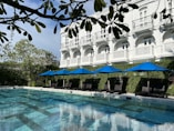 a large swimming pool with blue umbrellas in front of a white building