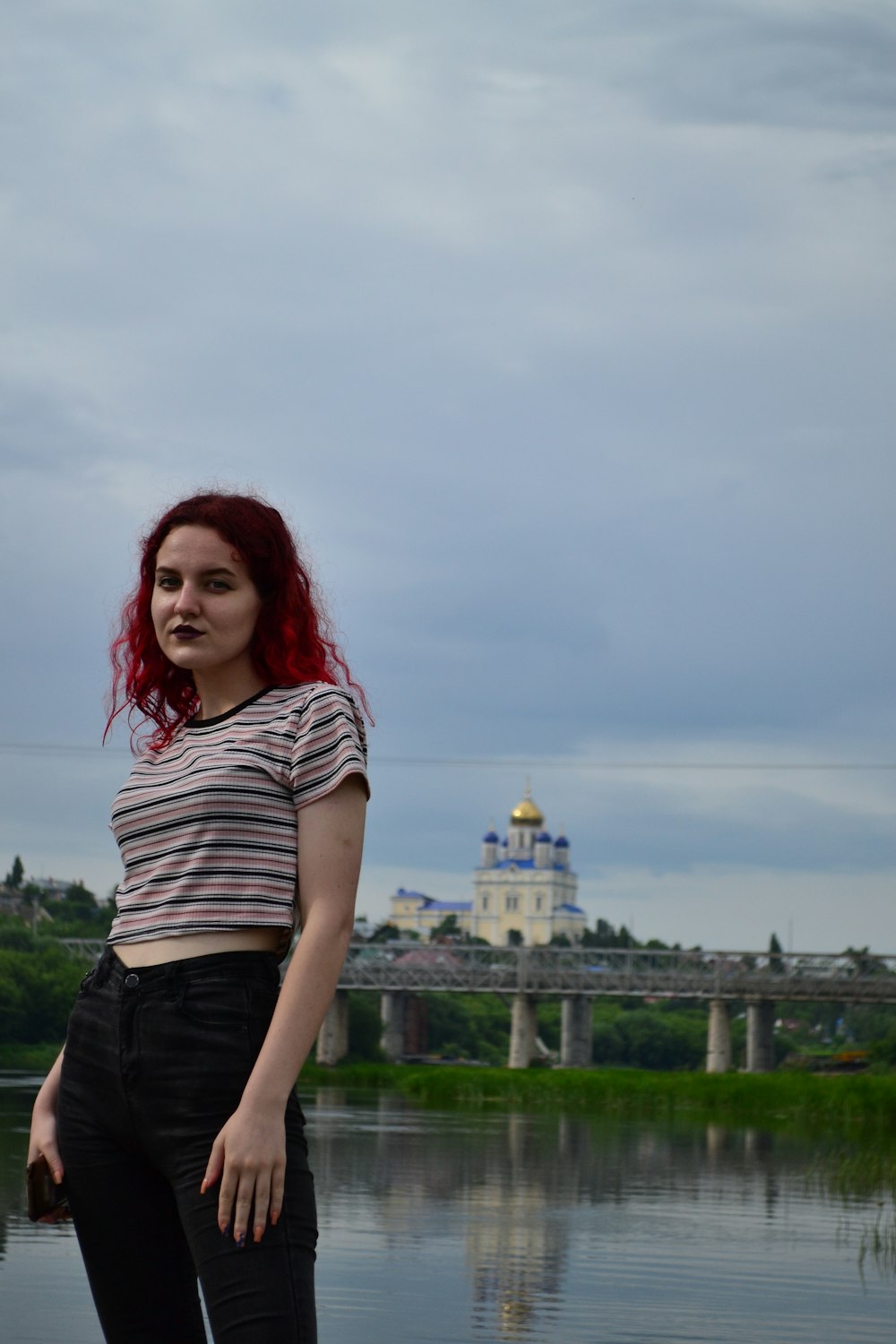 a woman with red hair standing in front of a body of water