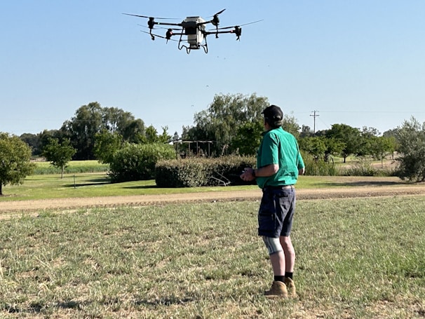 Operator controlling the drone from a shaded spot beside a tractor in a sunny field.