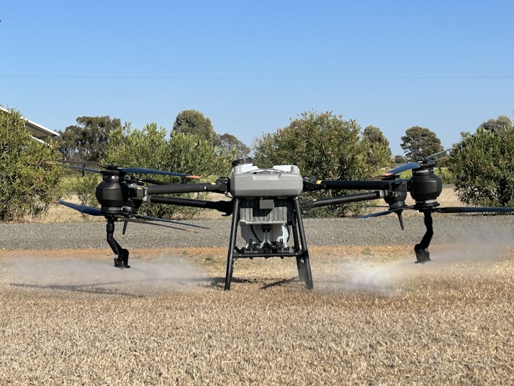 A drone flying low over a lush green pasture in western North Carolina, spraying fertilizer with precision.