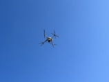A high-performance drone in flight against a clear blue sky.