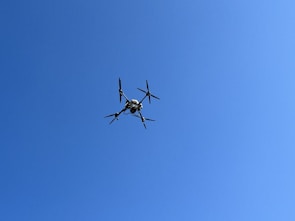 A high-performance drone in flight against a clear blue sky.