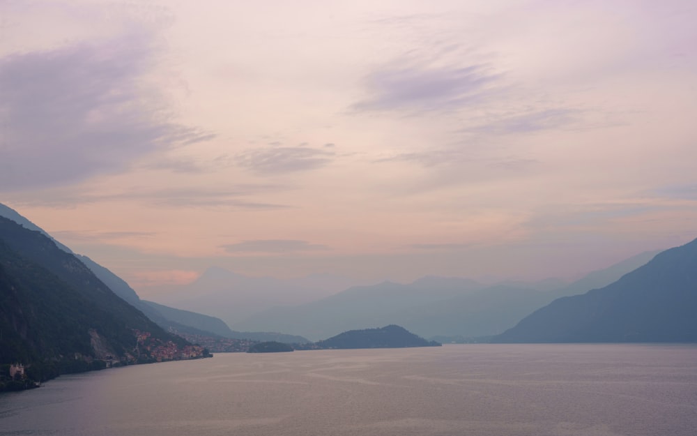 a body of water surrounded by mountains under a cloudy sky