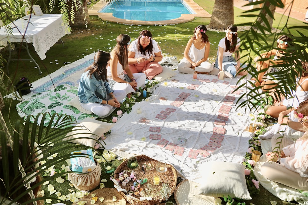 a group of women sitting on a blanket next to a pool