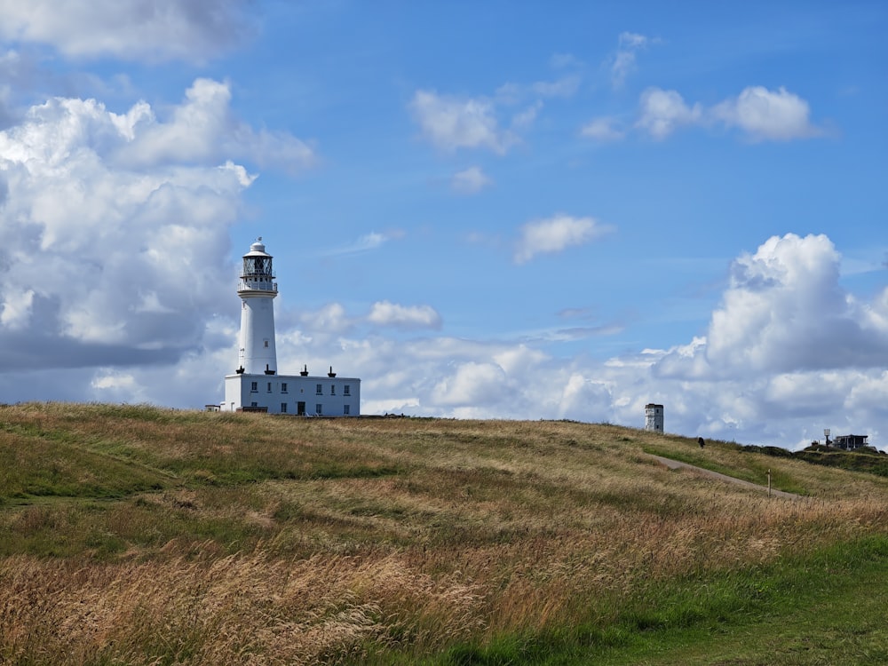 a white lighthouse on a grassy hill under a cloudy blue sky