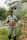 Photo of a cheerful man holding gardening tools, standing by a vegetable patch.