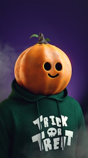 A person wearing a green hoodie with the words 'Trick or Treat' written on it. The person has a large, carved pumpkin as a head with a smiling face and a small stem and leaf on top. The background is dark purple with some mist or fog.
