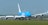 A large cargo airplane is taxiing on an airport runway. It features a bright blue and white color scheme and the words 'KLM Cargo' on its fuselage. The scene includes several wind turbines in the background against a clear blue sky, suggesting a modern and environmentally conscious setting.