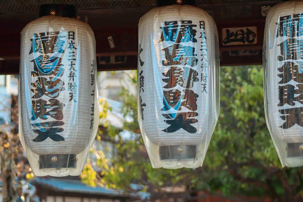 three lanterns with asian writing hanging from a roof
