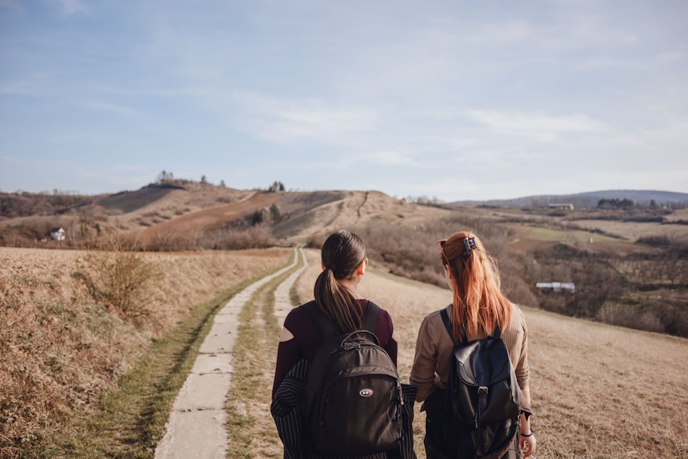 two women with backpacks walking down a dirt road