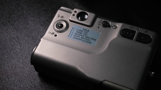 A close-up view of the back of a silver digital camera placed on a dark surface, featuring buttons, dials, and a label with the following text options: 'I LOVE YOU', 'THANK YOU', 'SEASONS GREETINGS', 'HAPPY BIRTHDAY', 'CONGRATULATIONS'.