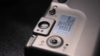 A close-up view of a section of an electronic device featuring a metallic surface with buttons and switches. A label is affixed to the surface, containing text for different greetings or messages. The layout suggests a customizable electronic message feature.