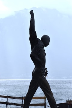 A silhouette of a statue depicting a person with one arm raised triumphantly against a backdrop of misty mountains and a body of water. The scene conveys a sense of strength and achievement, with muted colors and a serene landscape.