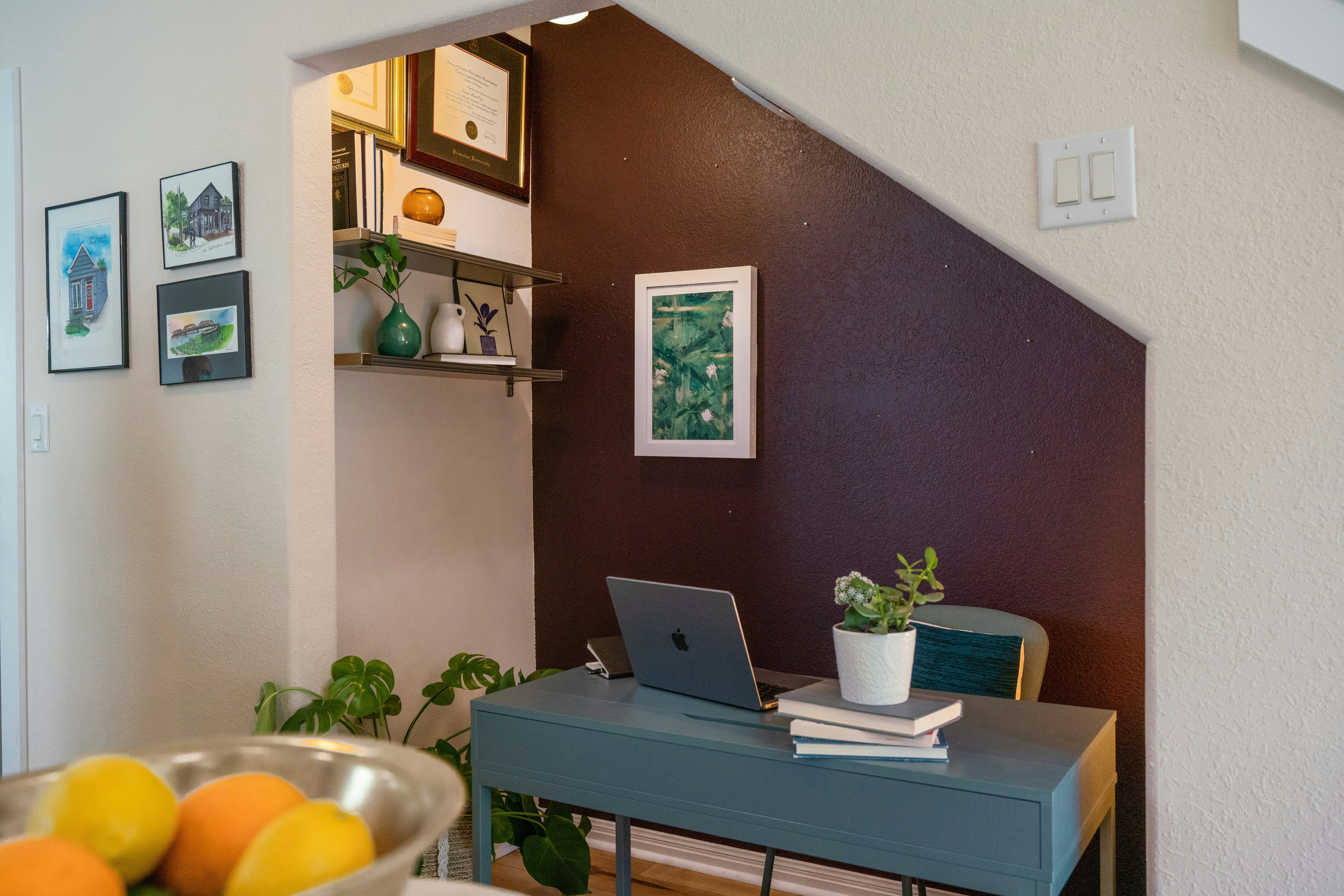 A view of a well-organized home office filled with essentials such as frames, indoor plants, books, and artworks.