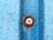 A weathered metal surface with a blue textured pattern is shown. In the center, a rusty screw with a circular metal washer is embedded.