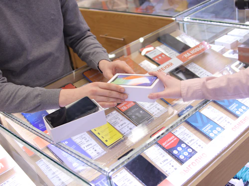 Shop assistant handing a boxed mobile phone to a customer across a display counter