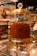A glass jar with a gold-colored lid filled with a large quantity of saffron strands. The jar is elegantly designed with decorative elements and a crystal-like handle on top. It is placed on a glass shelf surrounded by other spice containers and small boxes.