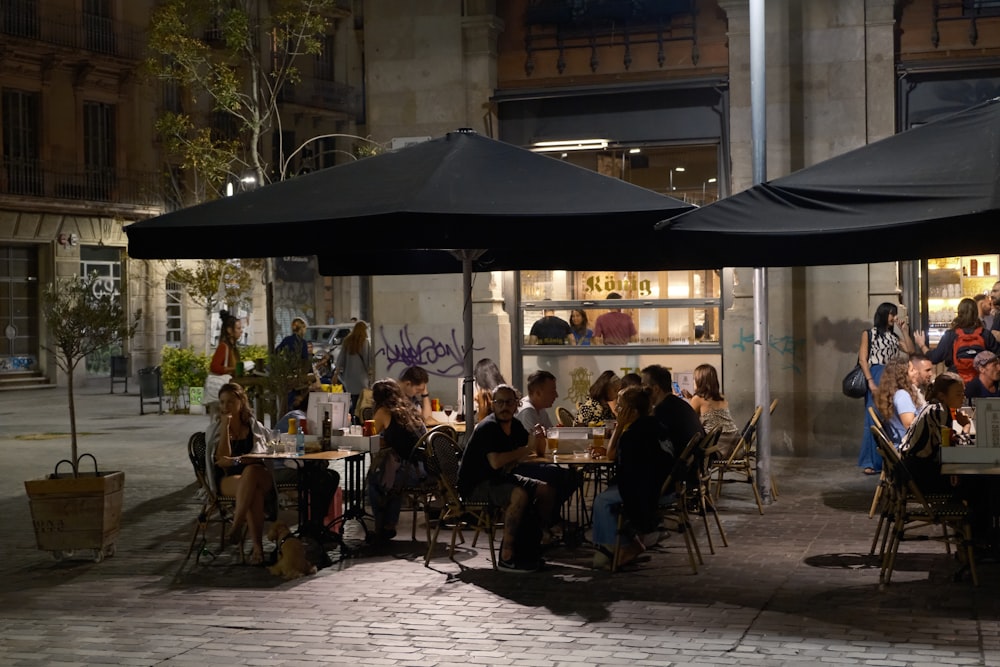 a group of people sitting at a table under black umbrellas