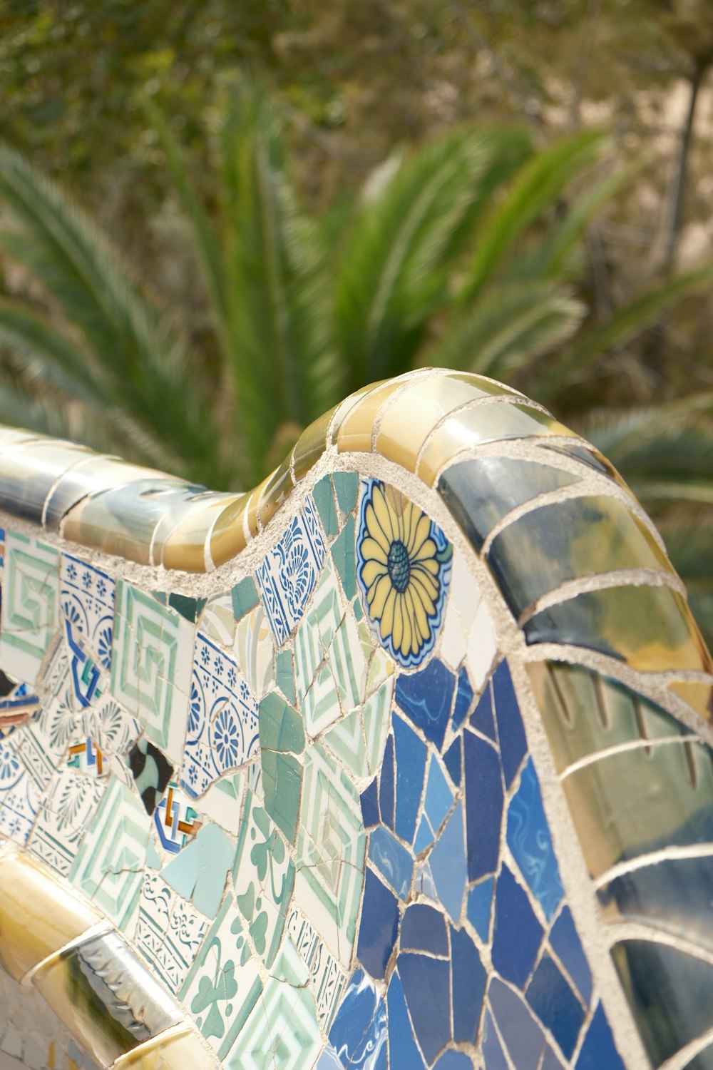 a close up of a tiled bench with a tree in the background