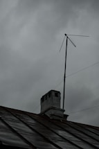 A rooftop with a weathered chimney and an old television antenna against a backdrop of overcast gray clouds, suggesting an impending storm or rain.