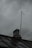 Technician fixing chimney flashing on a residential roof with storm clouds in the background.