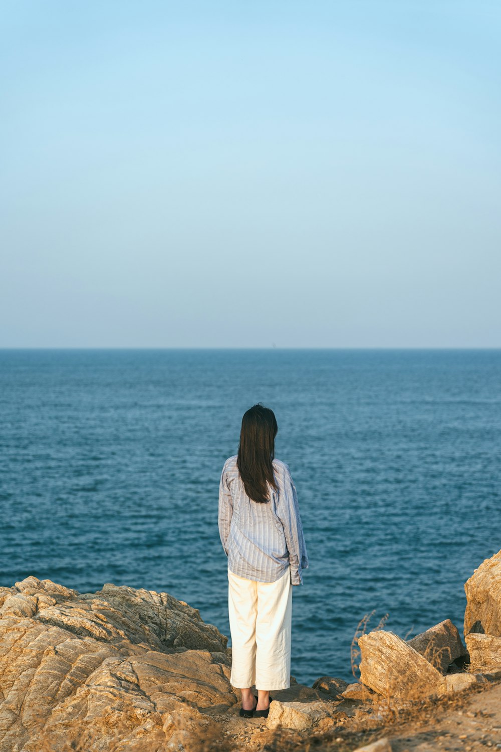 a woman standing on top of a rock next to the ocean