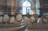 A miniature architectural model showcases abstract, geometric trees and buildings under soft lighting. The setting appears to be indoors, with an arched window in the background allowing natural light to filter through, creating a calm and contemplative atmosphere.
