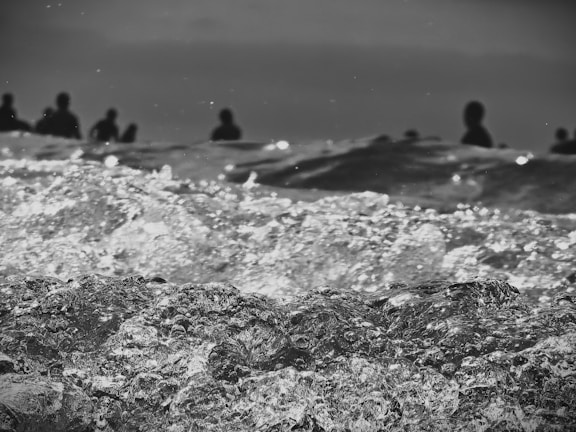 Waves captured in motion with a focus on the texture and details of the water. In the background, silhouettes of people stand out against the horizon, giving the scene a dramatic and mysterious feel.