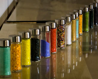 Array of colorful liquid powders in clear bottles arranged neatly on a wooden shelf, catching the light.