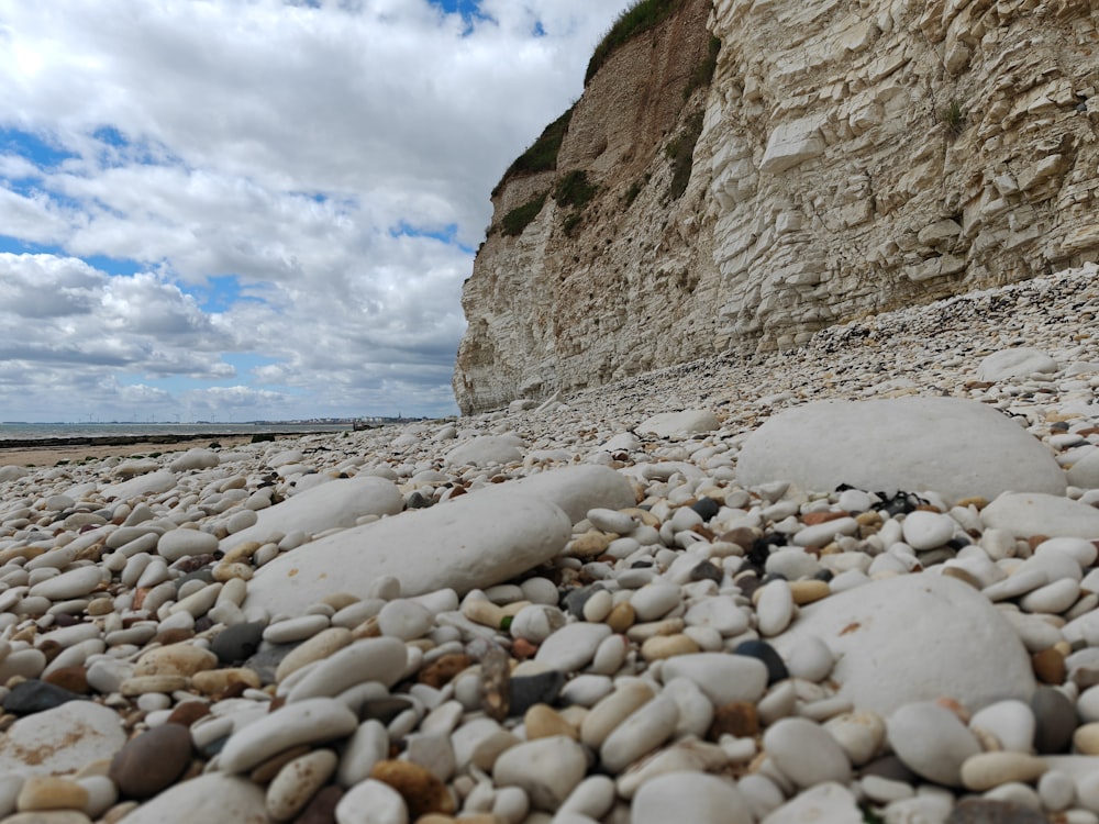 a rocky beach next to a cliff under a cloudy sky