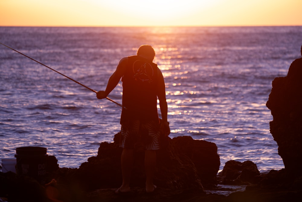 a man standing on top of a rock next to the ocean