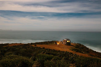Golden hour light bathing a coastal campsite where a man relaxes next to his van.
