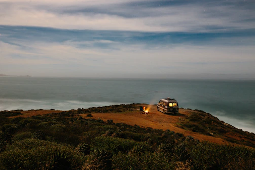 Golden hour light bathing a coastal campsite where a man relaxes next to his van.