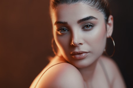 A close-up of a smiling woman gently applying elegant makeup in natural light.